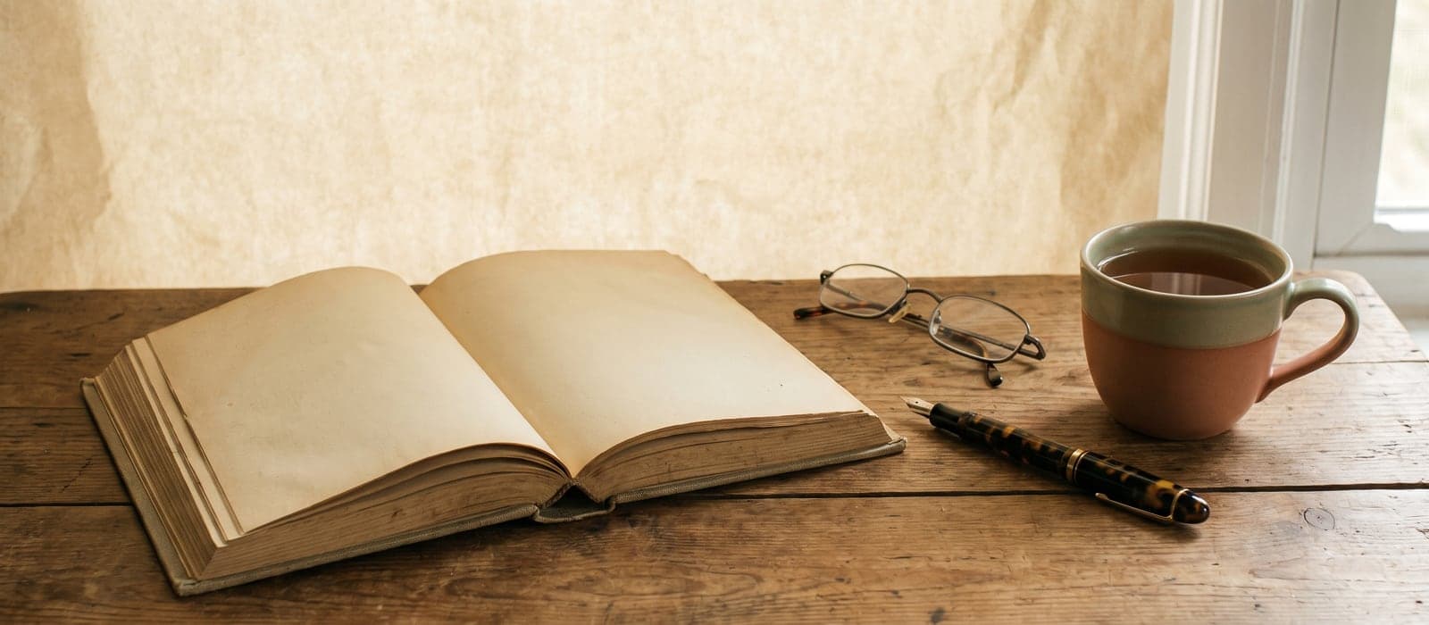 Open casebook with fountain pen, reading glasses, and tea on a desk