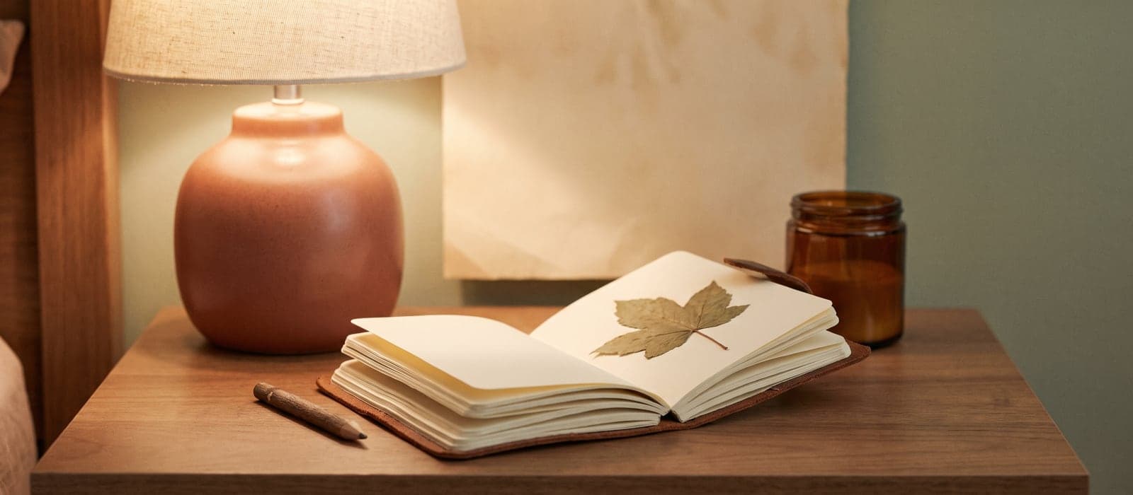 Pocket notebook with pencil and a pressed leaf in soft lamplight
