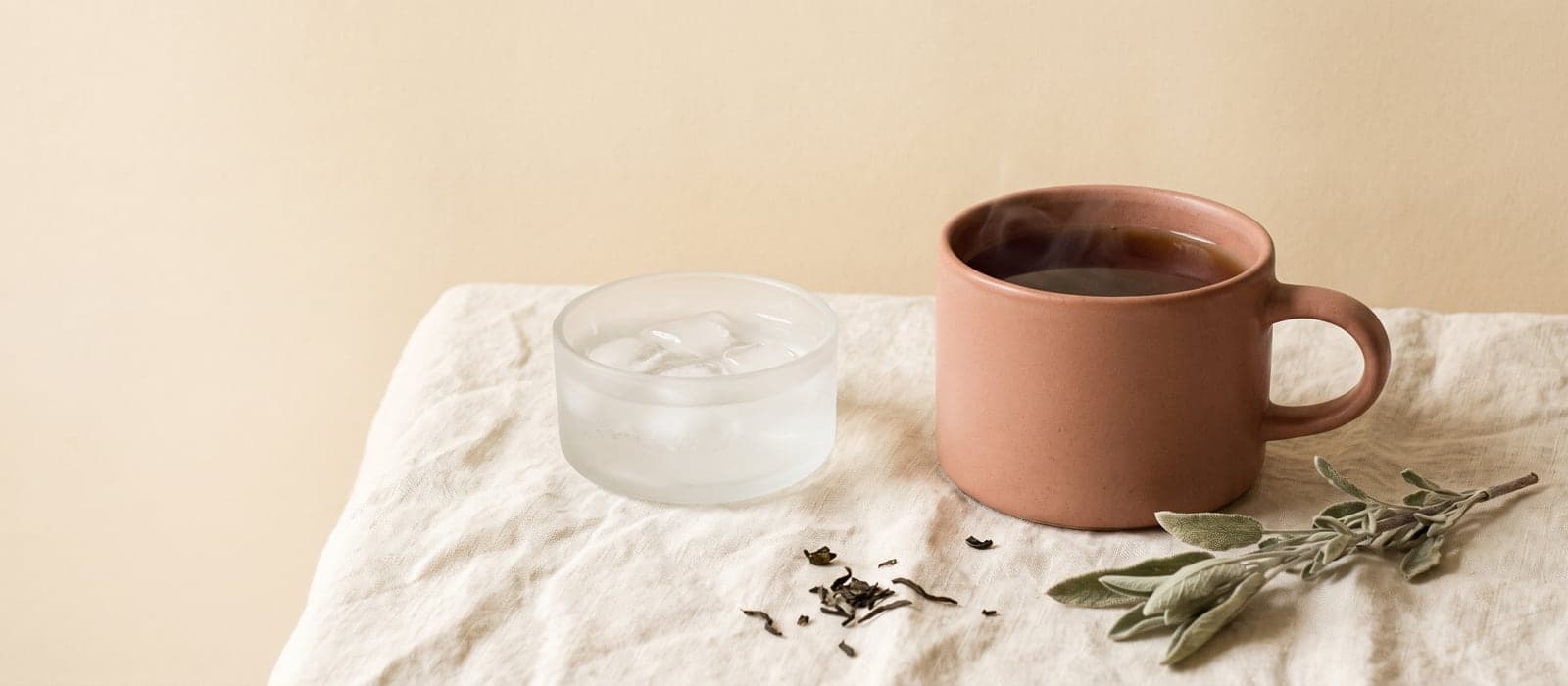 Steaming teacup beside a small dish of ice water on linen