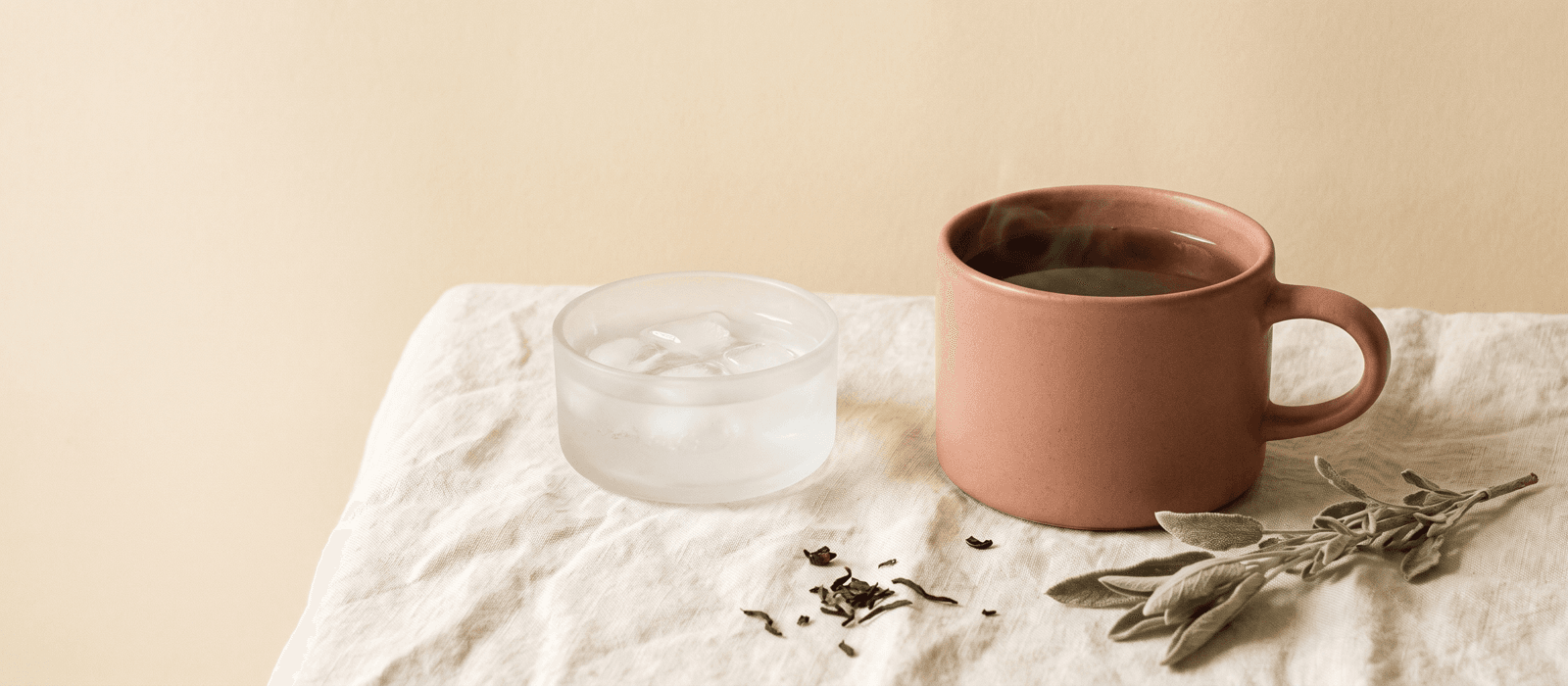 Steaming teacup beside a small dish of ice water on linen