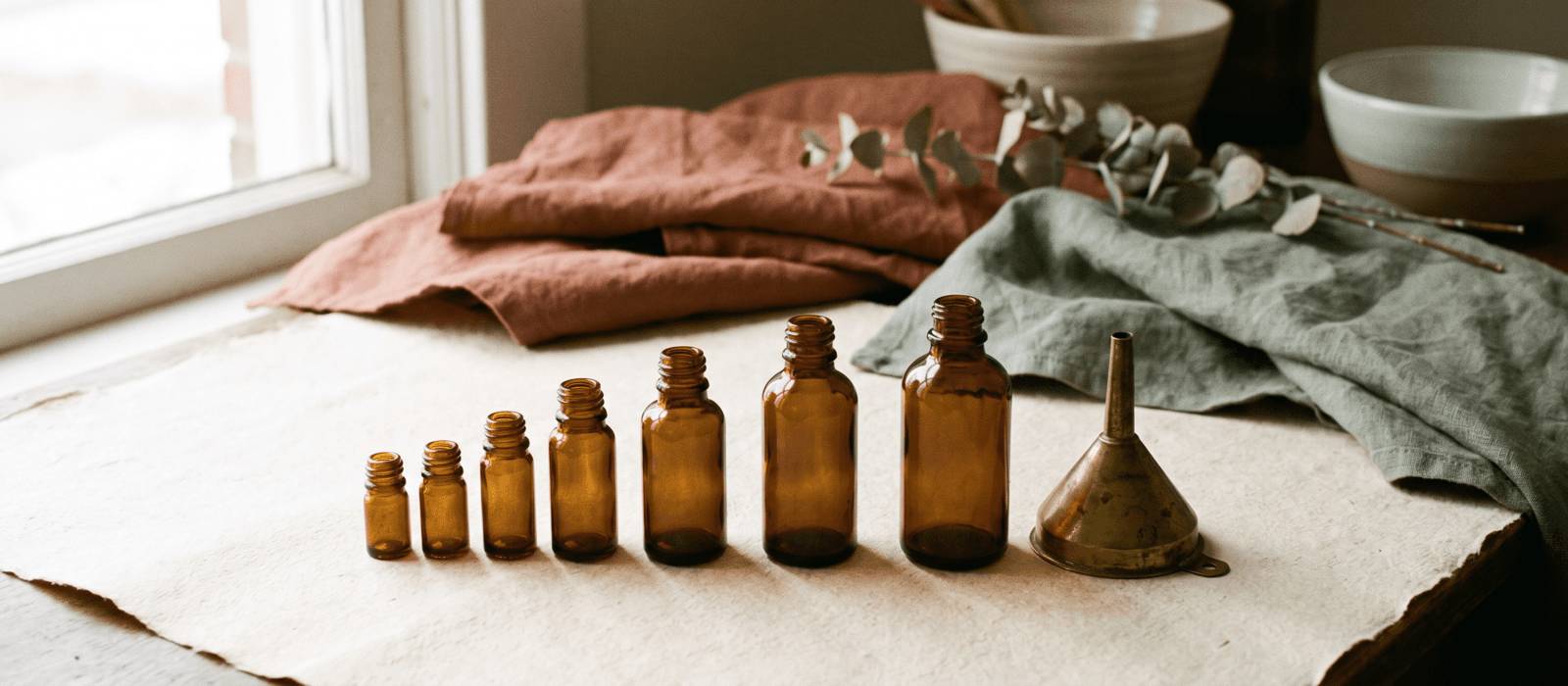 Row of amber glass bottles in ascending sizes with a brass funnel