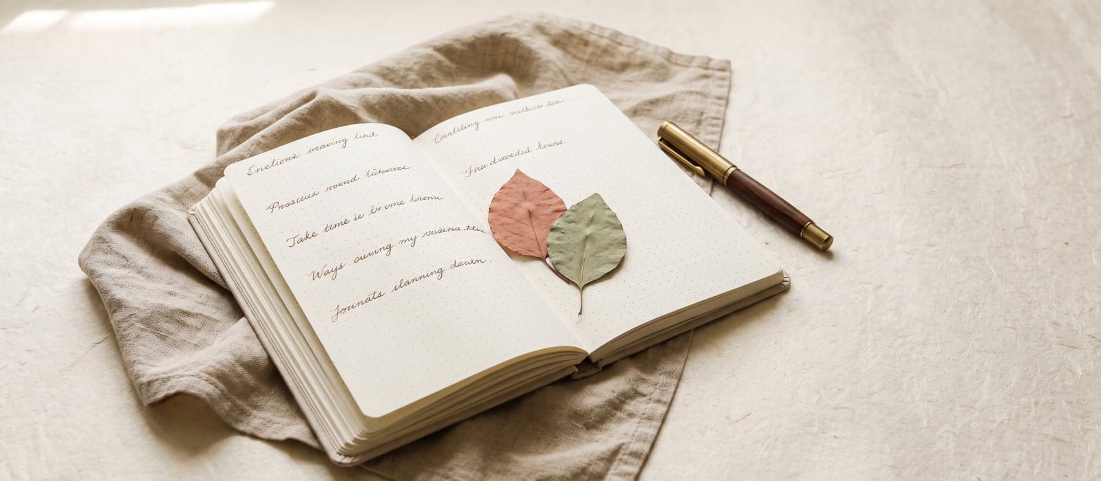 Open notebook with a fountain pen and pressed leaves on a linen cloth