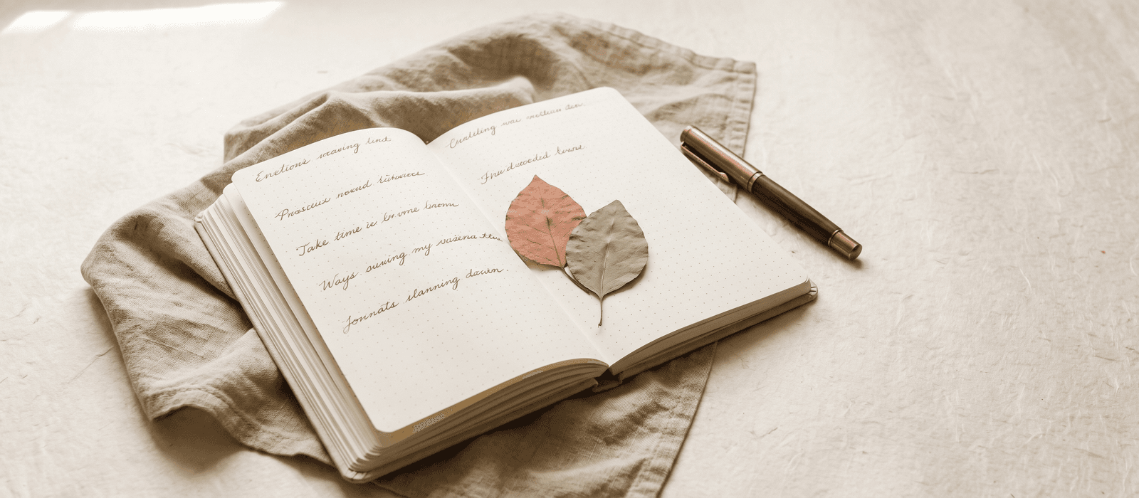 Open notebook with a fountain pen and pressed leaves on a linen cloth